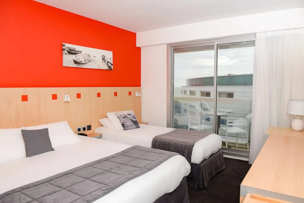 Chambre de l’Hôtel Cœur Marin aux Sables-d’Olonne : deux lits, mur orange et baie vitrée ouvrant sur un balcon