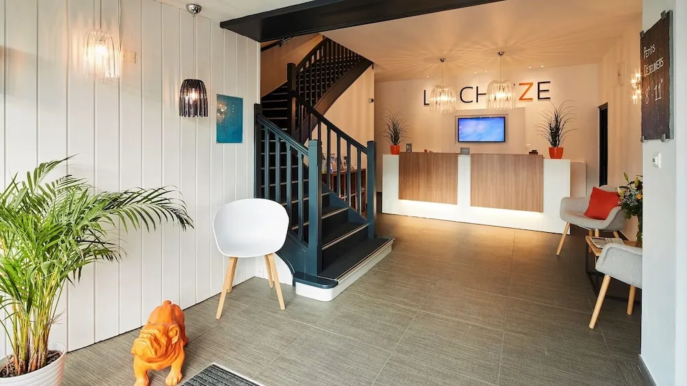 Accueil de l’hôtel La Chaize à Noirmoutier-en-l’Île : comptoir en bois, escalier, murs blancs et plantes vertes