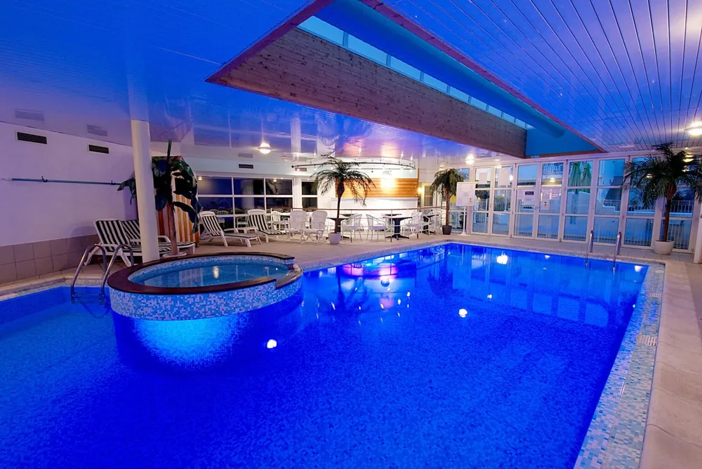 Piscine couverte de l’hôtel Le Robinson à Saint-Jean-de-Monts : bassin éclairé en bleu, spa, palmiers et baies vitrées
