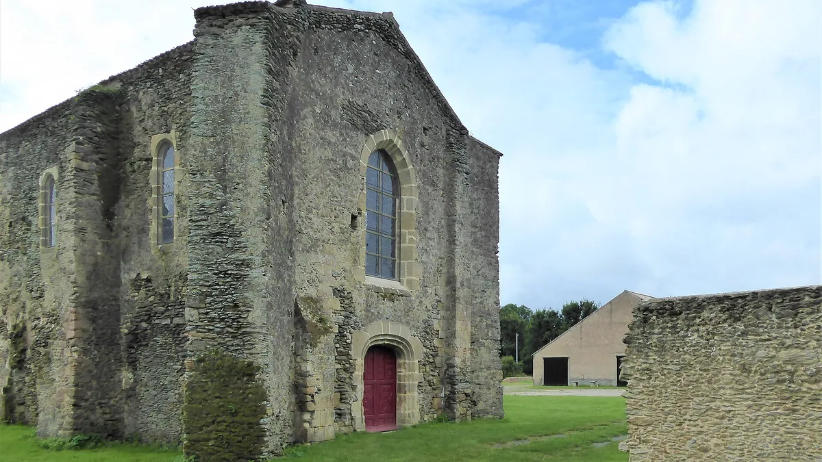 La chapelle de la commanderie de Coudrie à Challans, en pierre, avec sa porte rouge et sa haute fenêtre sous un ciel nuageux
