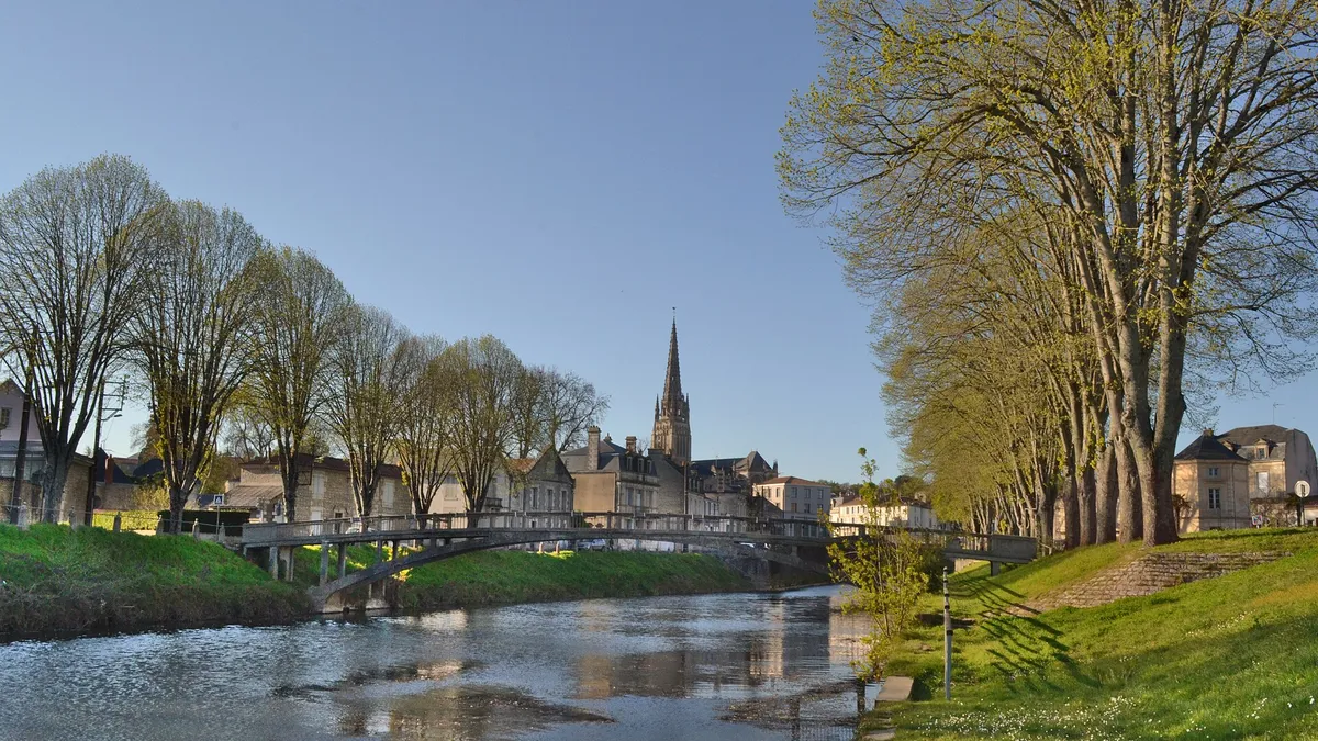 La rivière Vendée à Fontenay-le-Comte, bordée de maisons en pierre et d'arbres, avec la flèche de l'église Notre-Dame au loin