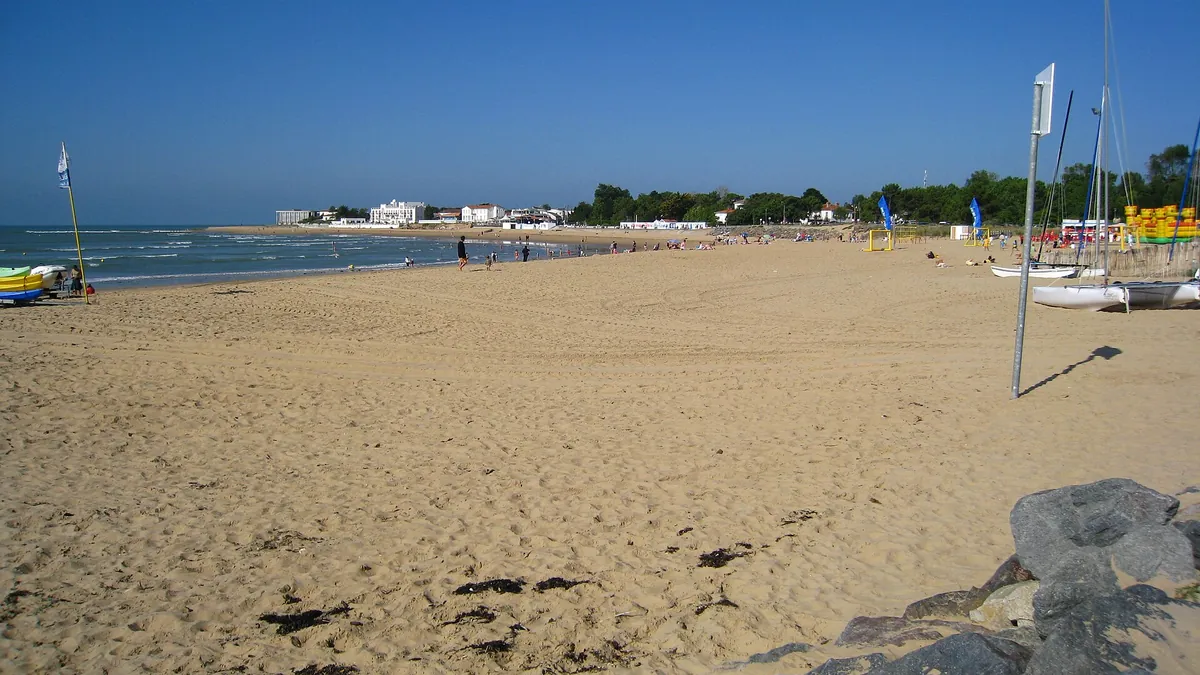 La plage centrale de La Tranche-sur-Mer, sable doré et bateaux de plage sous un ciel bleu, avec les bâtiments du front de mer au loin
