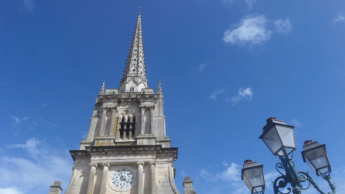 Le clocher de la cathédrale de Luçon, avec son horloge, sa flèche et un lampadaire, sous un ciel bleu