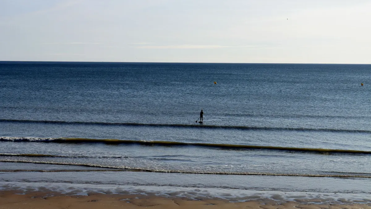 Plage de sable et océan Atlantique à Saint-Jean-de-Monts, avec un pratiquant de paddle au loin, un décor où dormir à Saint-Jean-de-Monts