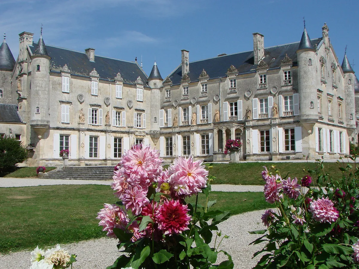 Façade en pierre claire du château de Terre-Neuve, à Fontenay-le-Comte, avec ses tourelles, sa pelouse et des dahlias au premier plan