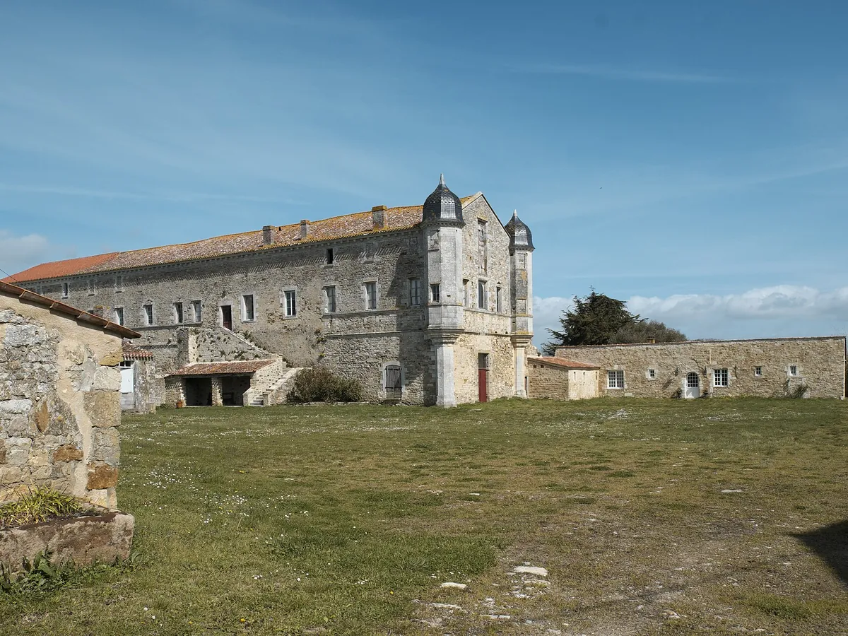Bâtiments de pierre de l'abbaye de Lieu-Dieu à Jard-sur-Mer, sous un ciel bleu, avec un pré au premier plan