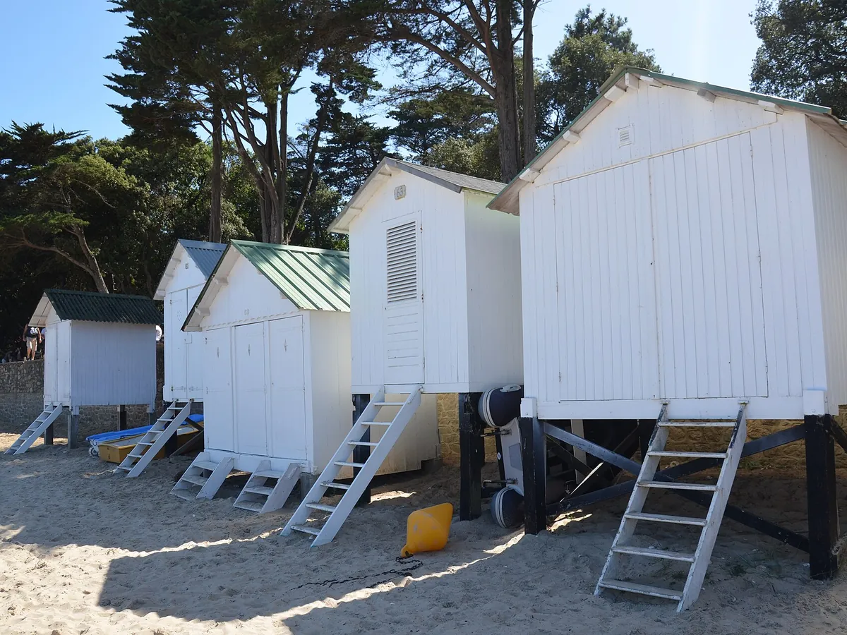 Cabines de plage en bois blanc sur pilotis, sur le sable de la plage des Dames, sous les pins du Bois de la Chaise à Noirmoutier-en-l'Île