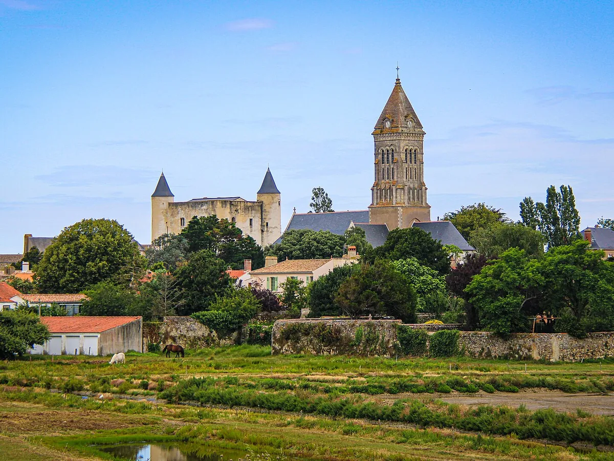 Château de Noirmoutier aux tours pointues et clocher de l'église Saint-Philbert, derrière des arbres et des prés, à Noirmoutier-en-l'Île