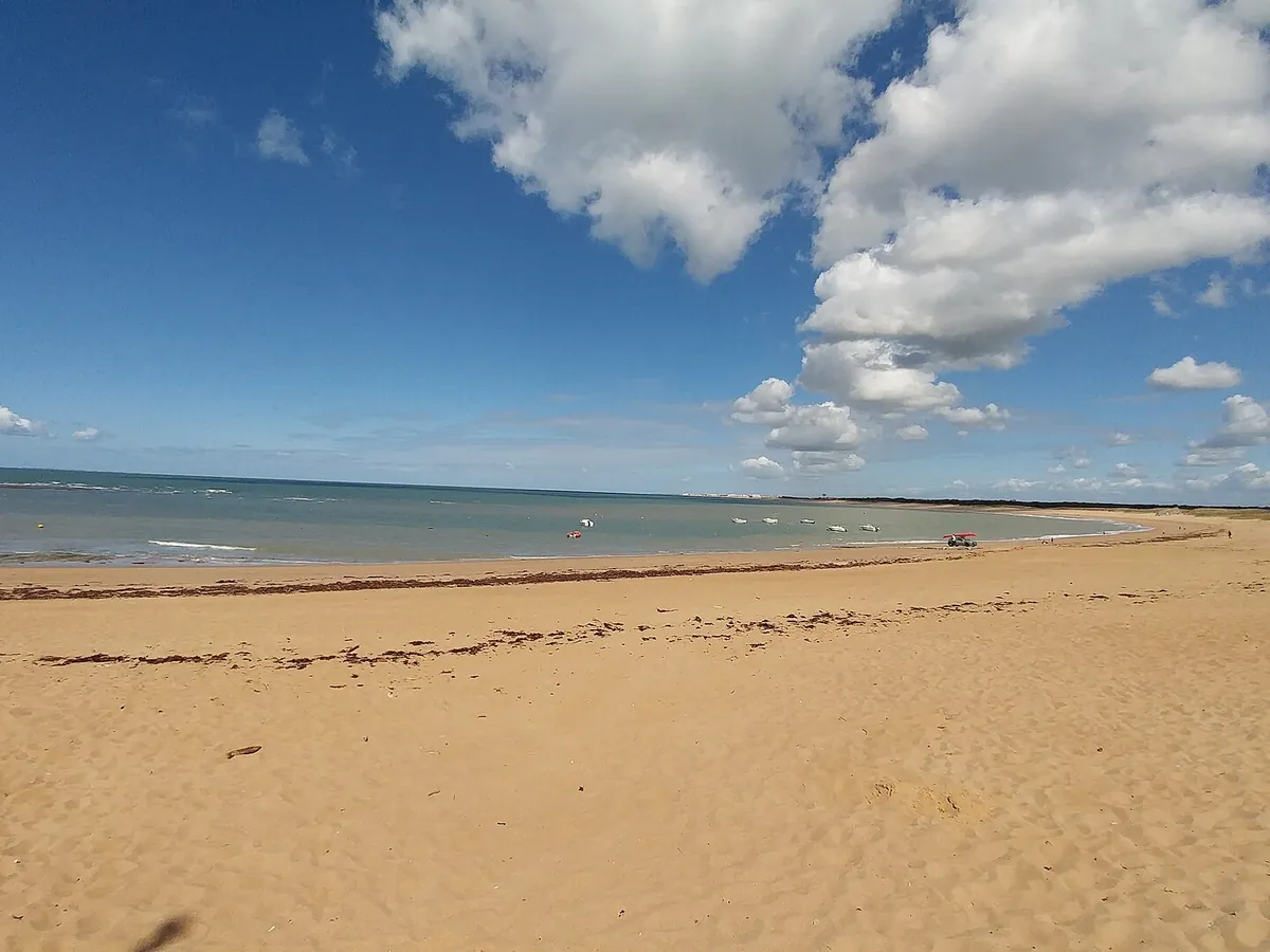 Grande plage de sable de Sion-sur-l'Océan sous un ciel bleu, avec quelques bateaux au loin sur la mer