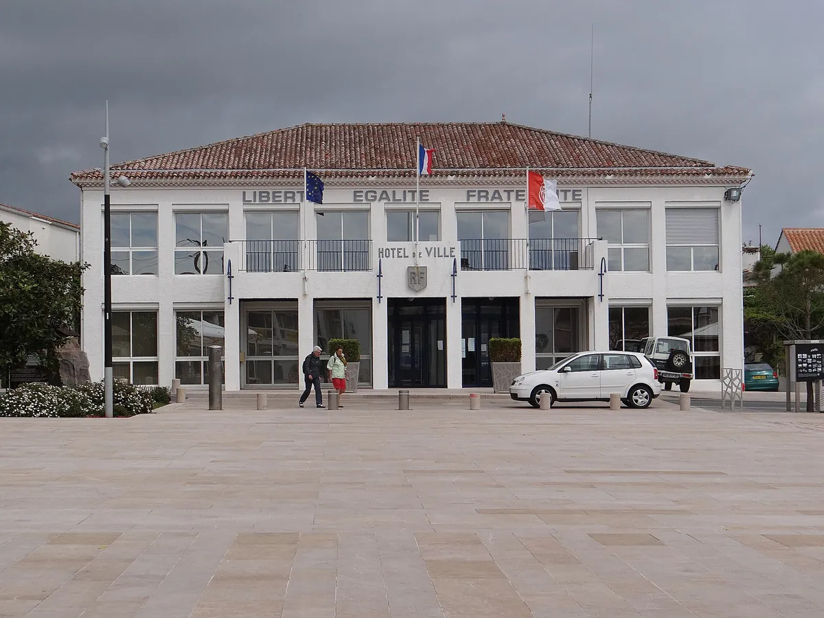 L'hôtel de ville de La Tranche-sur-Mer, bâtiment blanc à toit de tuiles orné de drapeaux, sur une place dallée